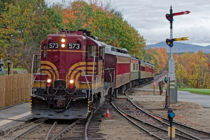 Vintage train number 573 on tracks with autumn trees and signal post in background.