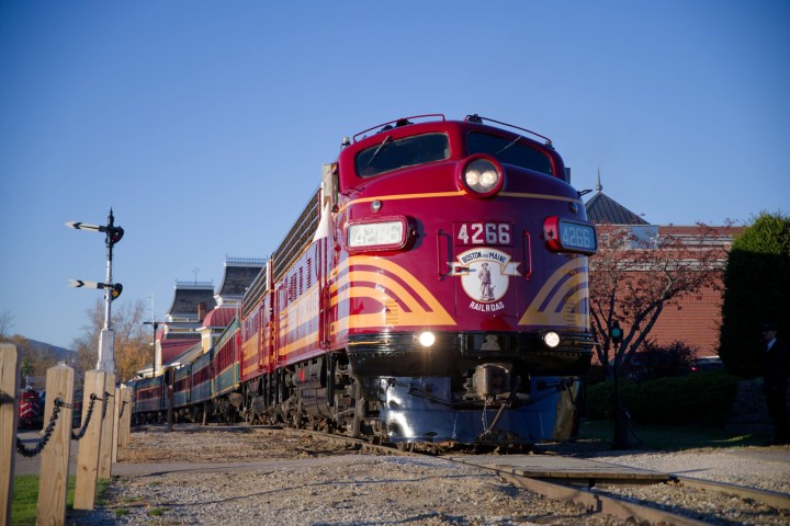 Red vintage train on tracks near a station building under clear sky.