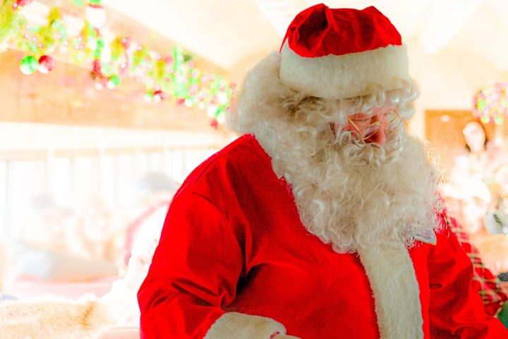 Santa Claus walking through a decorated train car filled with passengers.