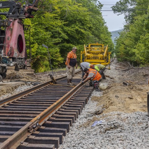 Workers in safety vests installing train tracks with construction vehicles nearby.