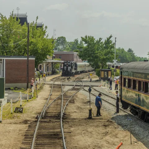 Train station with tracks, people, and Conway Scenic Railroad train on the right.