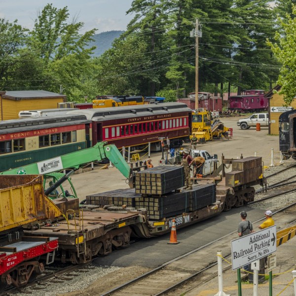 Train yard with workers and various train cars, surrounded by trees.
