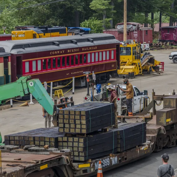 Railroad yard with a historic train and maintenance equipment, people working nearby.
