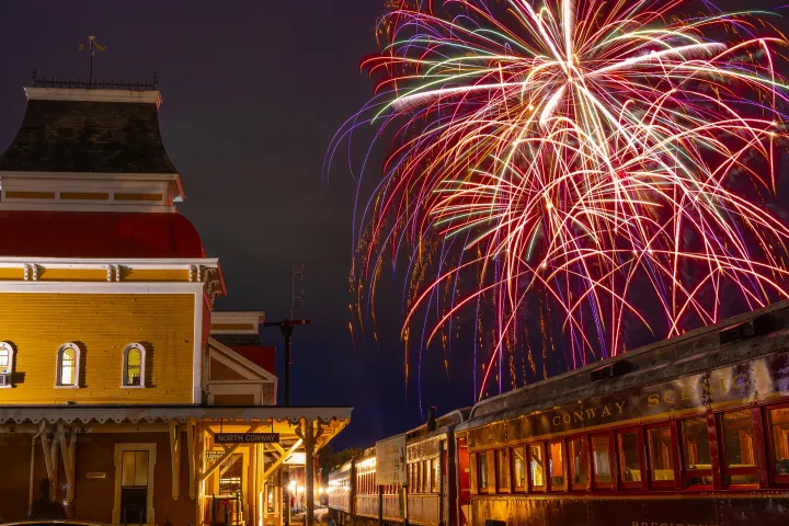 Fireworks above a vintage train and station building at night.