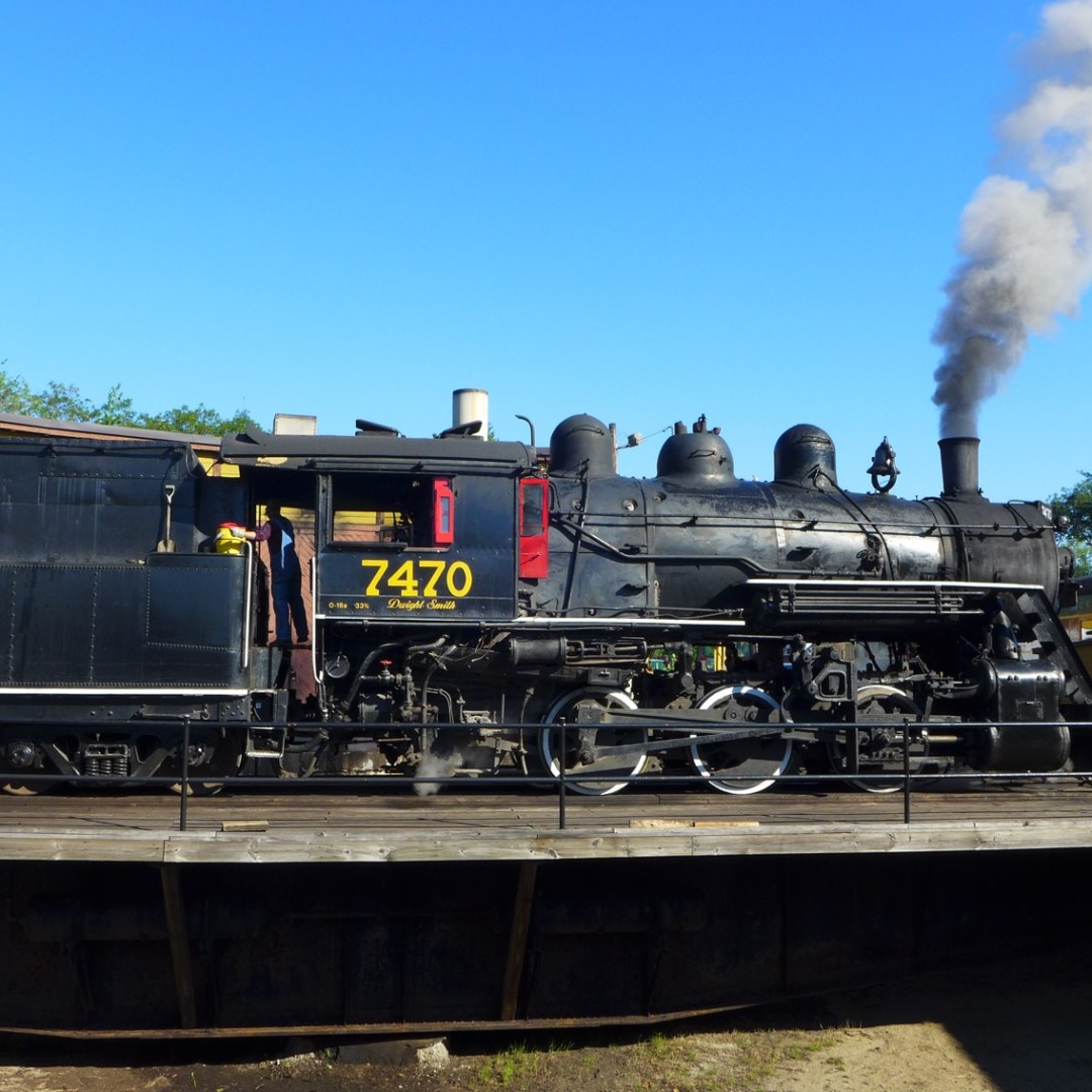 Steam locomotive 7470 on turntable with smoke, Conway Scenic Railroad sign visible.