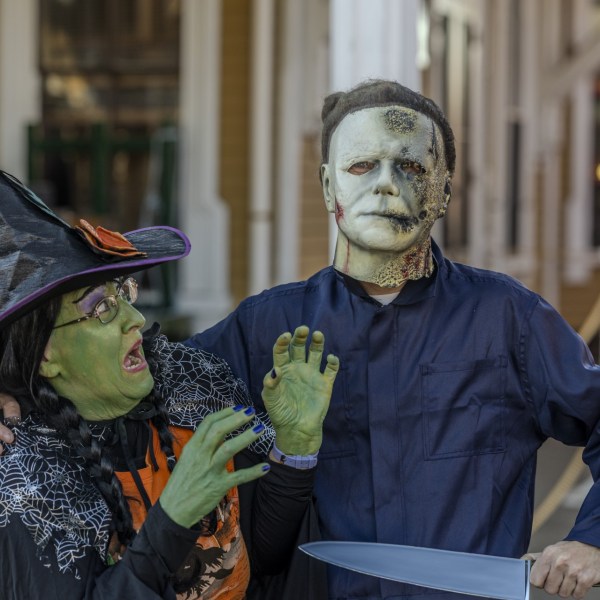Two people in Halloween costumes: a witch and a masked figure, standing together with a knife prop.