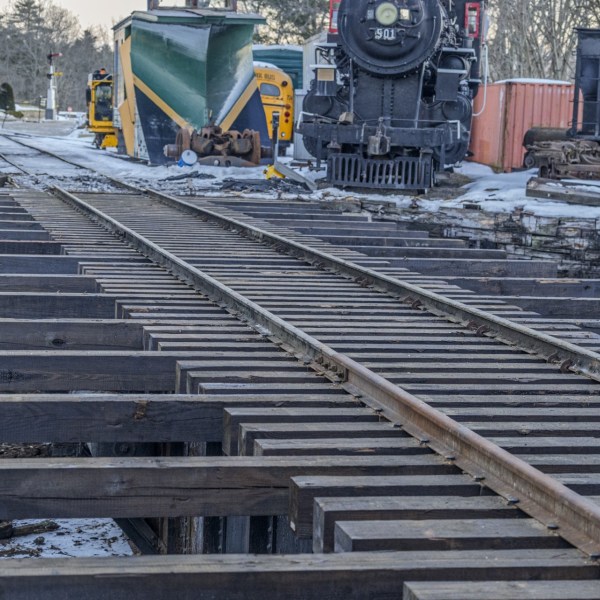 Railroad tracks under construction with snow and trains in the background.