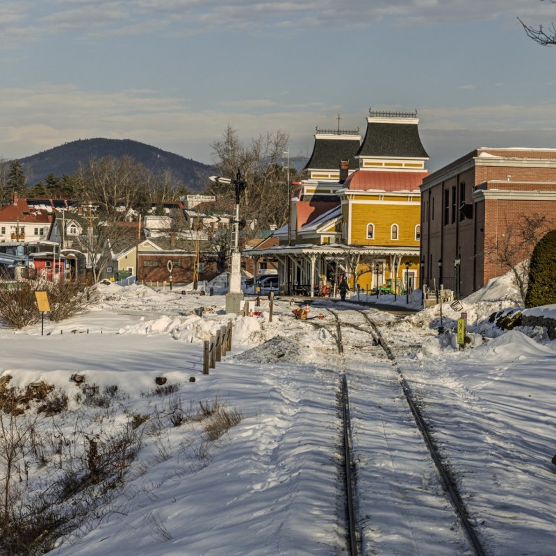 Snow-covered train tracks leading to a colorful town with mountains in the background.