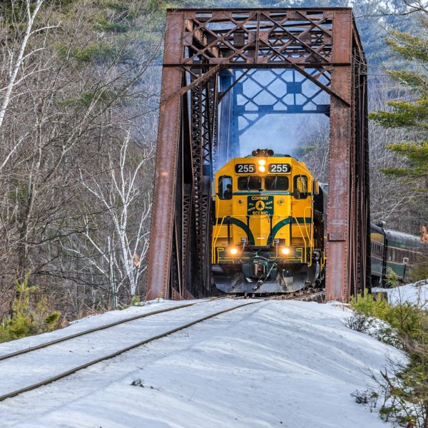 Yellow train crossing a rusty iron bridge in a snowy forest landscape.