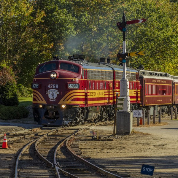 Vintage red train on tracks surrounded by trees under a clear sky.