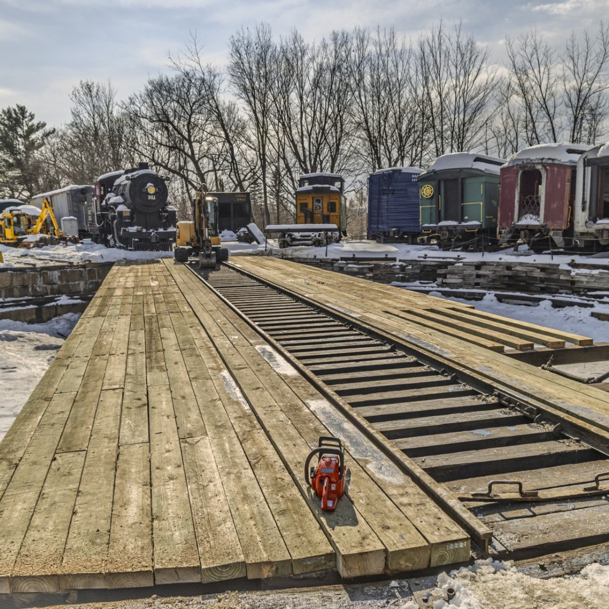 Wooden railway turntable with trains, snow, and a distant tree line.