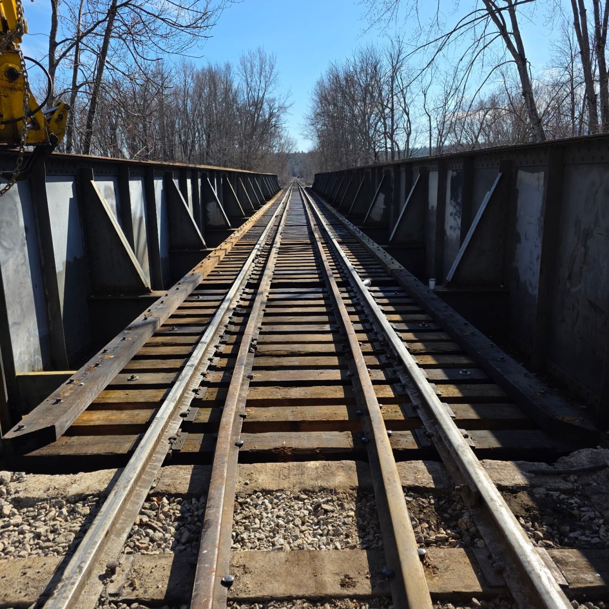 Railroad tracks on a bridge with bare trees on a clear day.