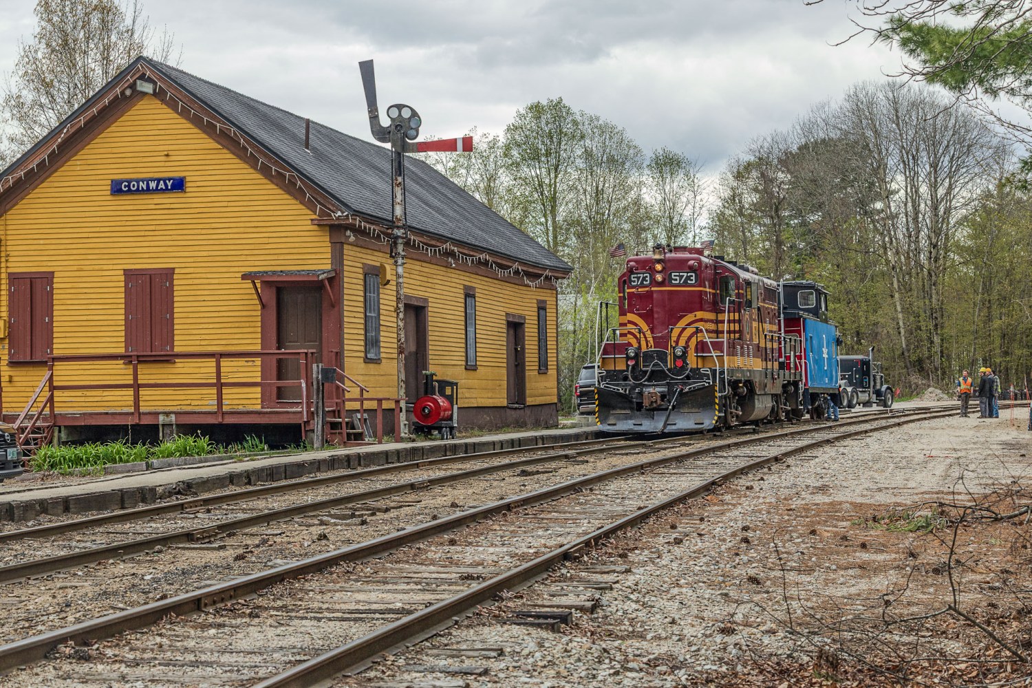 Vintage train by yellow station building with signs and trees.