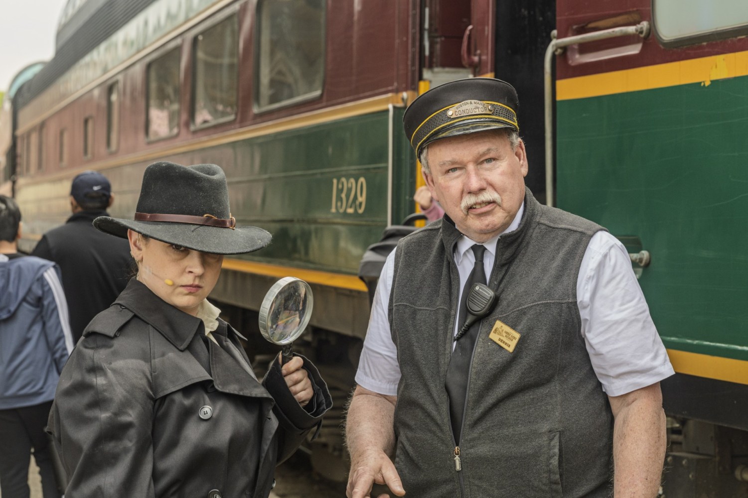 Person in detective outfit and train conductor by vintage train.
