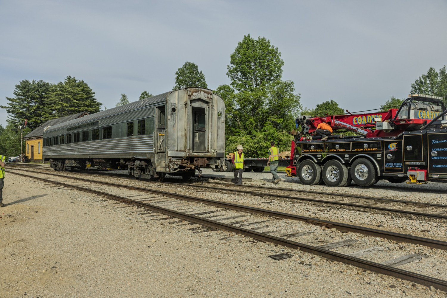 Train car being towed by a truck near tracks, with workers present.