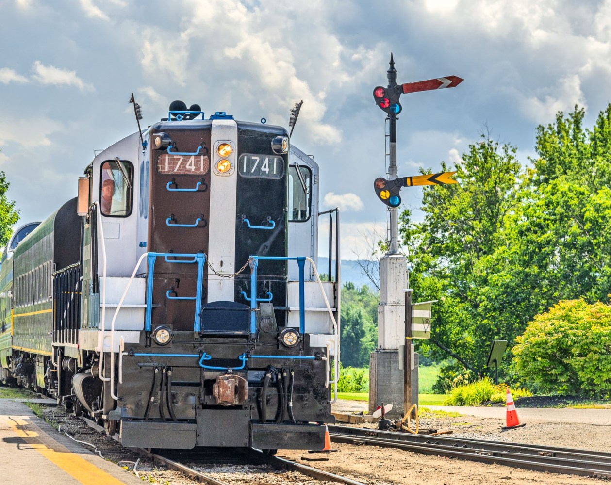 Train at station with semaphore signals and lush greenery.