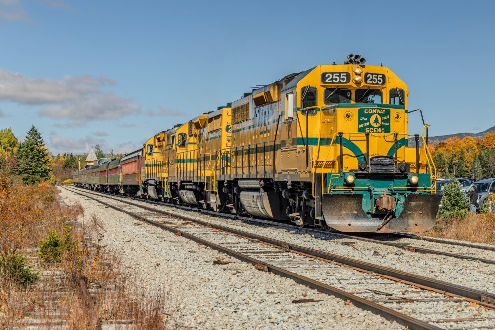 Two yellow and green locomotives pulling a train on a sunny day.