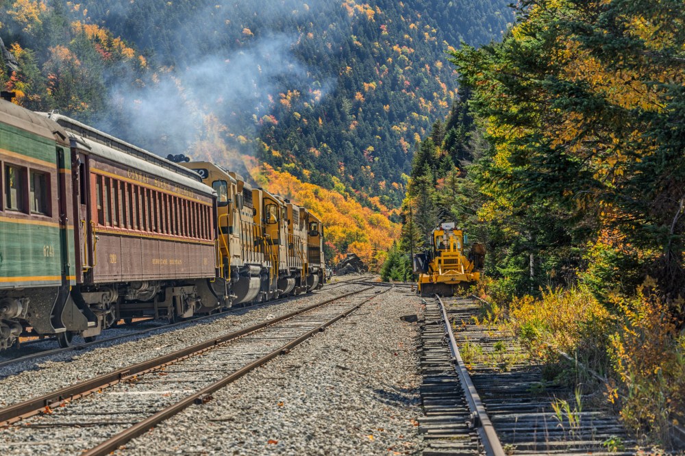 Train on tracks in a mountainous area with autumn foliage.